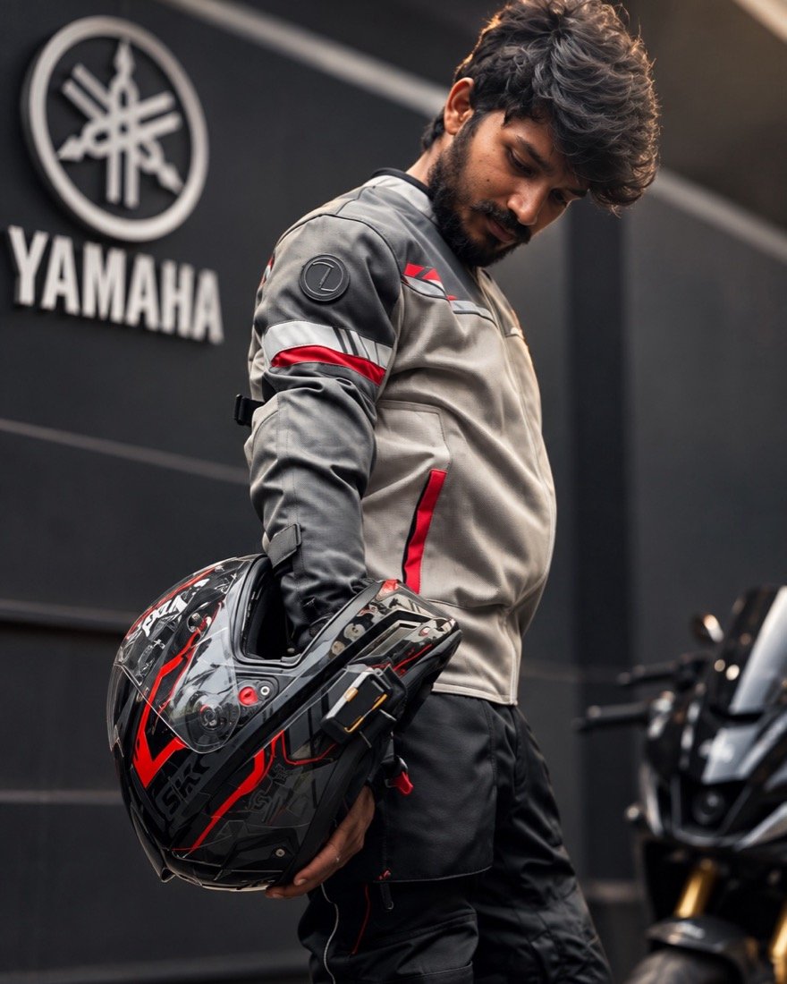 Deva, co-founder of Rahi, in riding gear holding his helmet beside his motorcycle