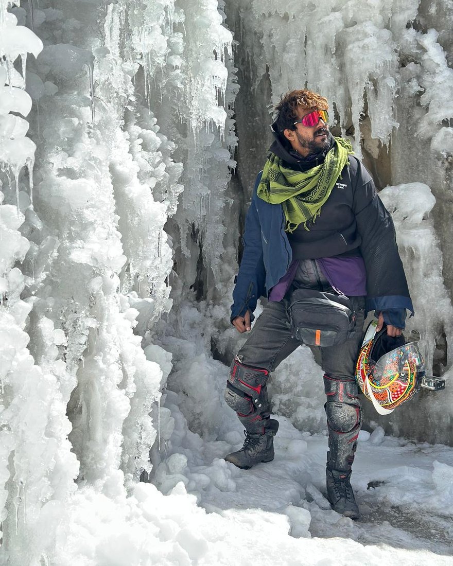 Yashas Prasad, co-founder of Rahi, in riding gear holding his helmet beside a frozen waterfall
