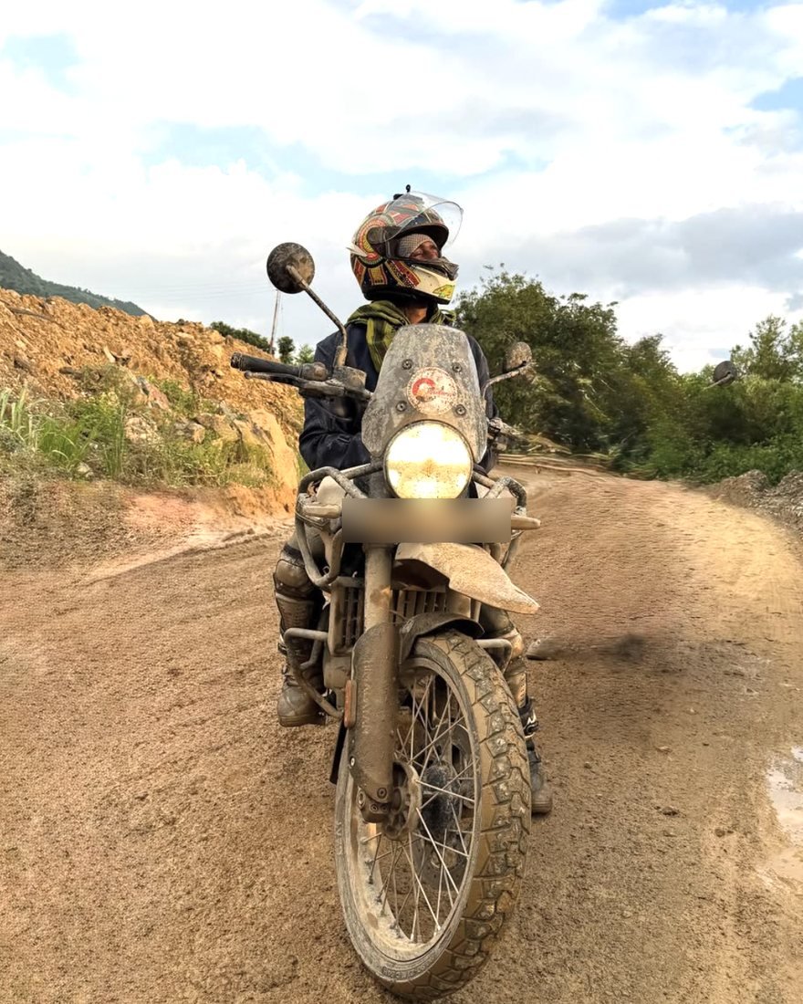 A rider in full gear on a mud-covered adventure motorcycle on a dirt mountain road
