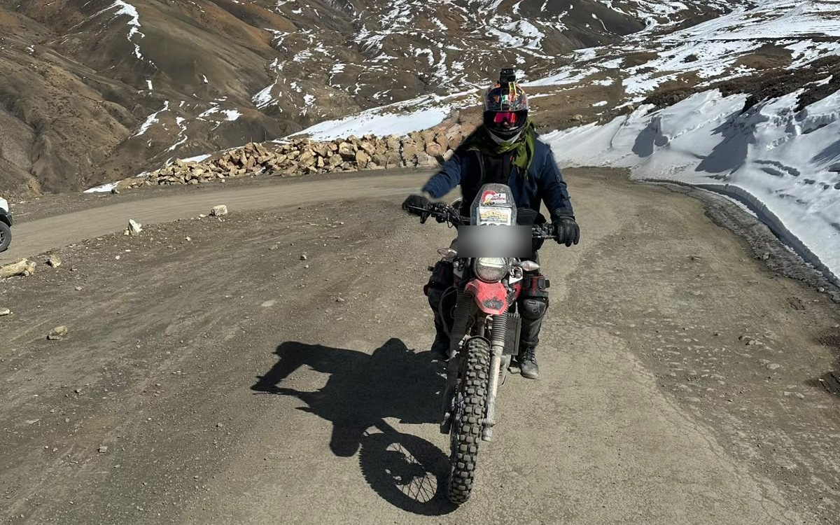 A rider in gear on a mountain road below a snow-covered peak