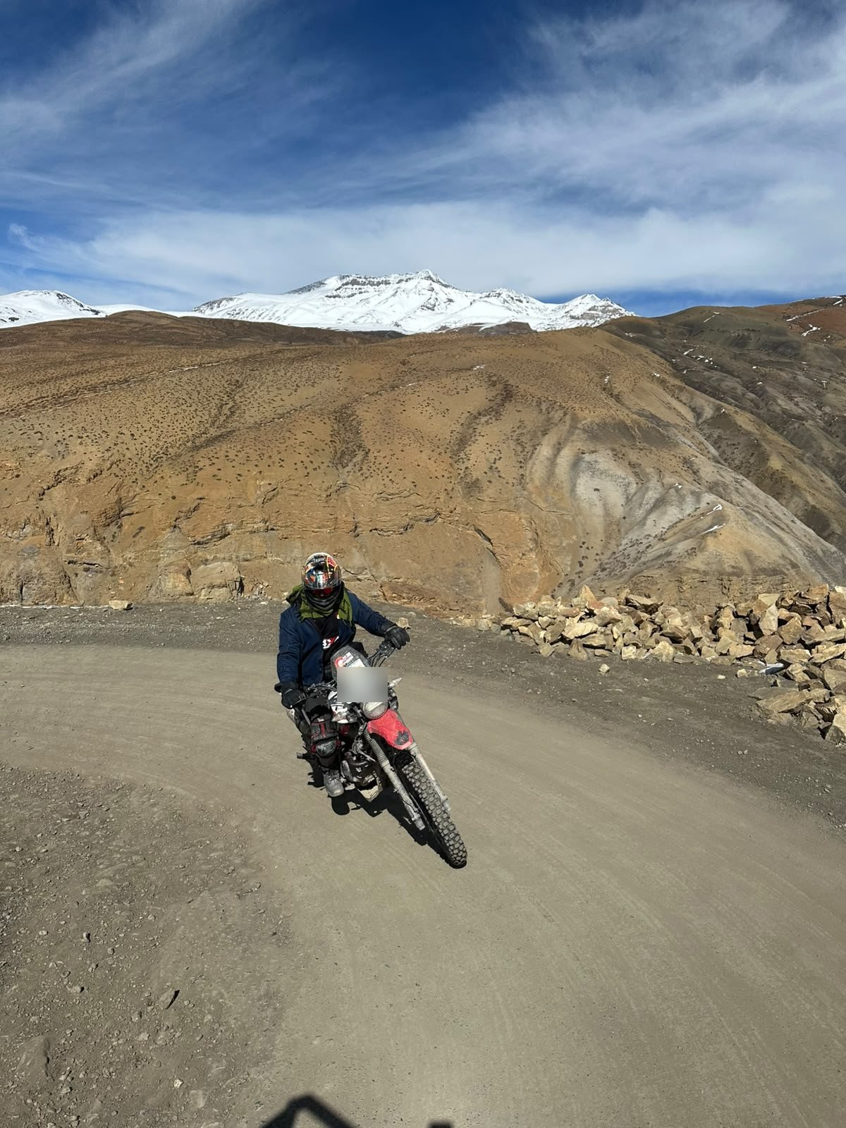 A rider in full gear taking a dirt-road bend on an adventure bike in Spiti