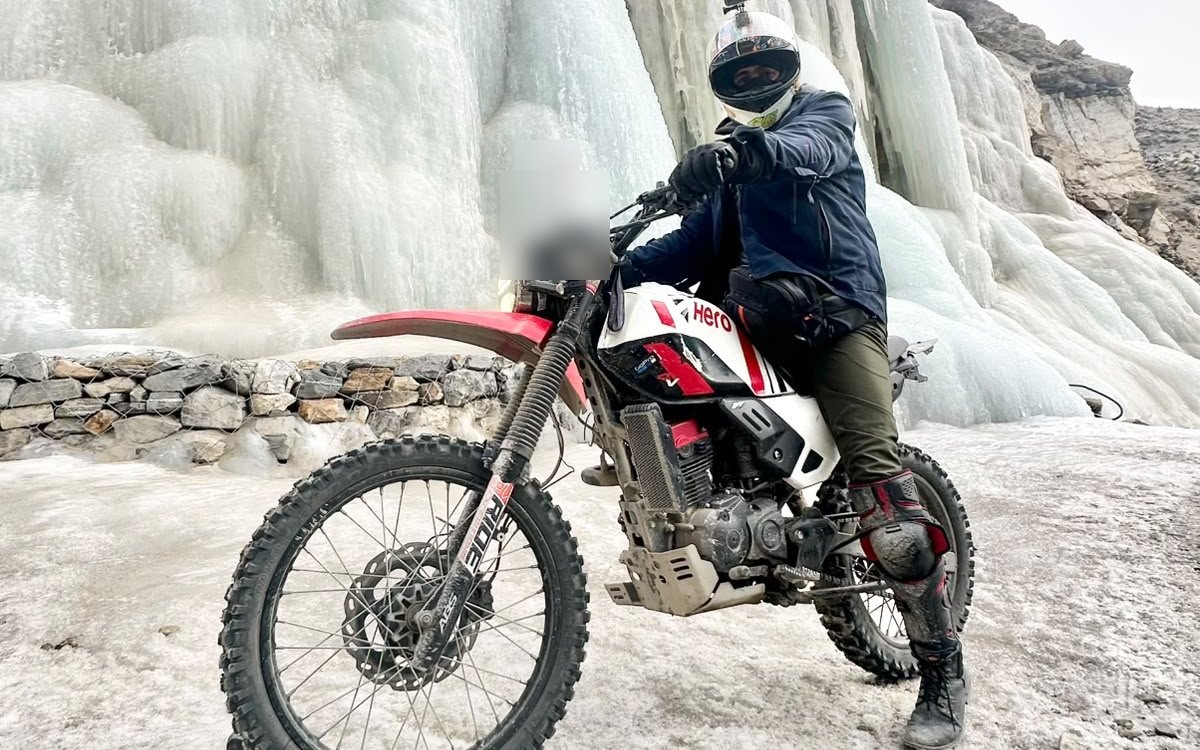 A rider in helmet and knee guards on an adventure bike in front of a frozen waterfall