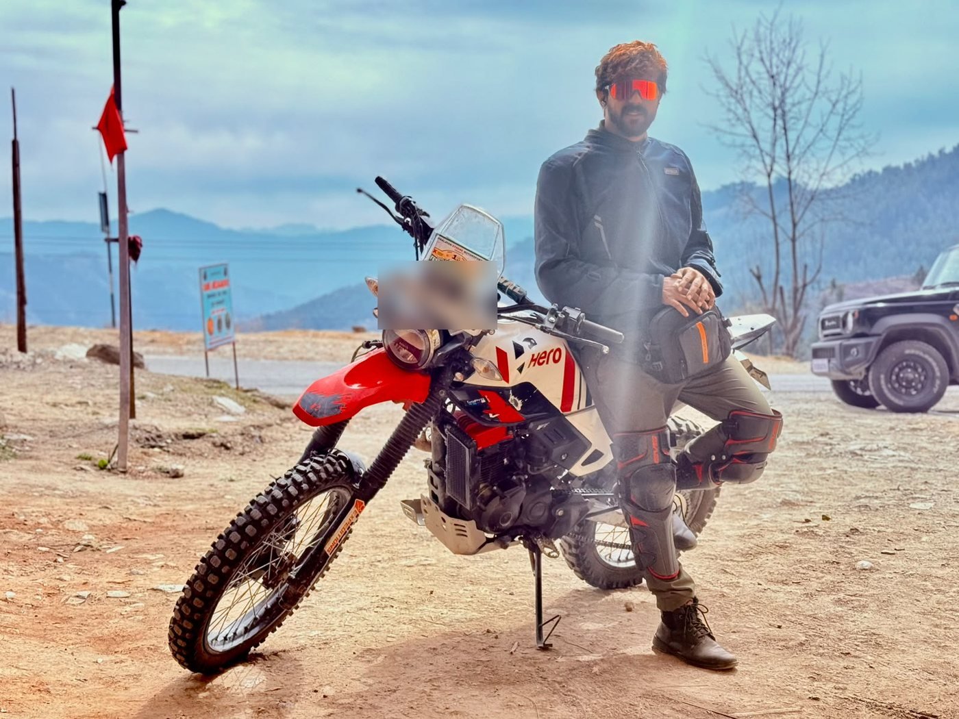 A rider in jacket and knee guards leaning on his rally-numbered adventure bike